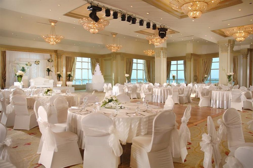 Sunrise Alex Avenue Hotel Alexandria Exterior photo The photo depicts an elegant banquet hall set up for a formal event, likely a wedding or reception. The room features several round tables covered with white tablecloths and adorned with floral centerpieces. Chairs are also dressed in white covers, c